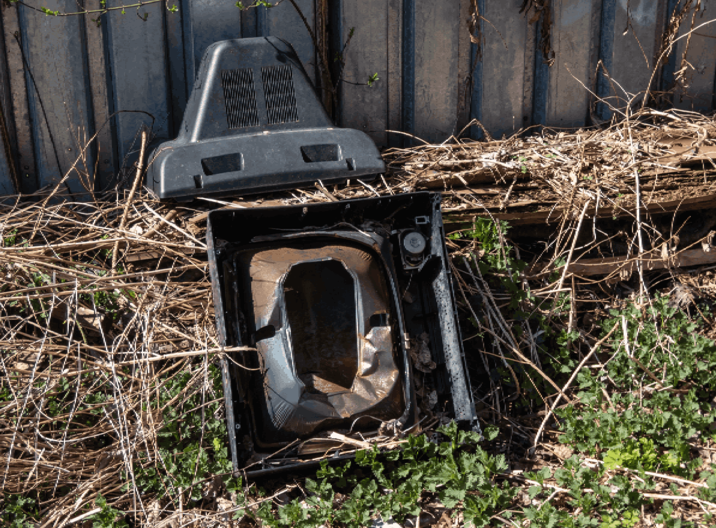 View of old tv broken into pieces thrown out in nature near a fence. Discarded electronics. Concept of pollution by illegal garbage, destruction of nature. Unrecycled